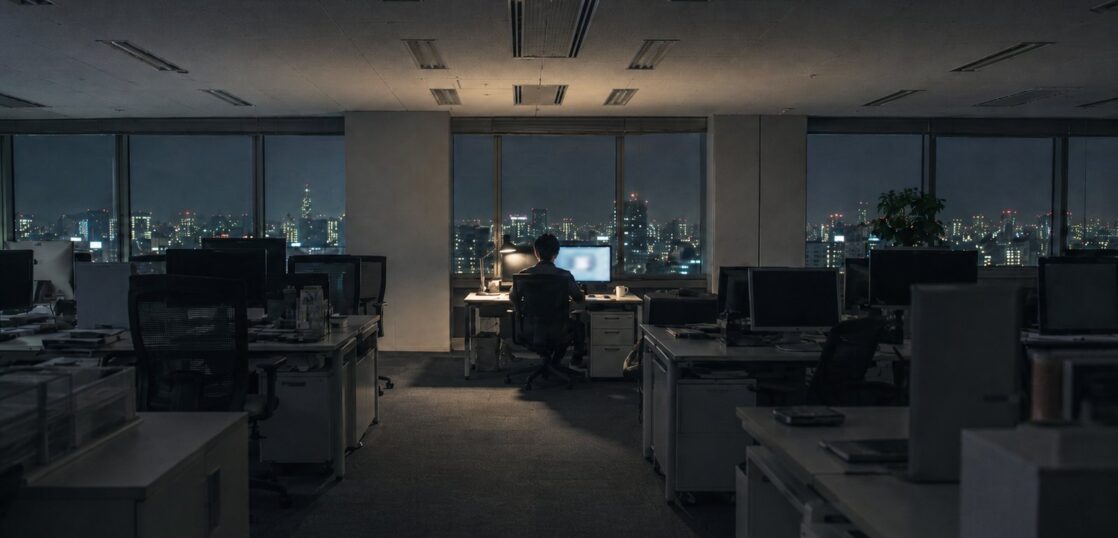 照明の落ちた深夜のオフィスで一席だけ灯るデスク